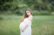 © Kristina89 - A beautiful young pregnant woman with curly long hair in a white dress walks in the field. Spring portrait of a pregnant woman. Happy pregnancy.