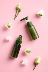 Wall Mural - Green spray bottle and dispenser on pink background with ice cubes and flowers. Natural cosmetics packaging design. Flat lay, top view.