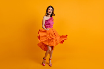 Poster - Lovely girl in colorful attire dancing with smile. Refined caucasian woman playing with her orange skirt.