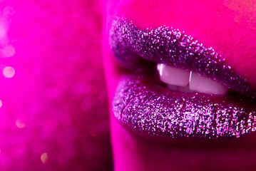 Fashion model with shiny sparkles on plump lips. Pink neon studio light. Macro view of woman with glamorous make-up. Nightlife, night club concept. Copy space.