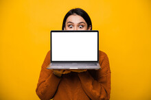 Portrait Of A Surprised Shocked Caucasian Young Woman, Hiding Behind Blank White Screen Laptop, Standing On Isolated Orange Background.