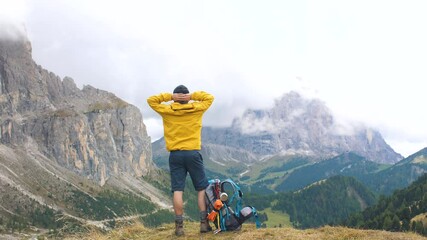 Wall Mural - young man hiker standing on mountain viewpoint with cloudy sky and fog. yellow jacket, backpack, bla