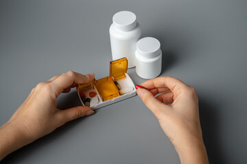 Wall Mural - Woman holding a pill in her hand. The young woman took the pill from the pill box. Healthy lifestyle. Pills on a gray background. Tablets for breakfast, lunch and dinner.