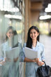 © Prathankarnpap - Portrait of asian businesswoman holding documents folder and  standing outside office building.