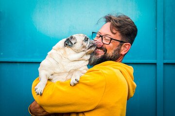 My best friend dog concept with funny scene adult man with beard and pug dog kissing him on the face - people and animals have fun and love together in friendship