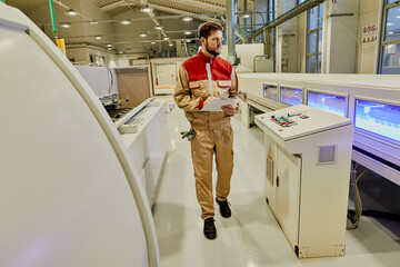 Wall Mural - Male worker taking notes while supervising automated machines at woodworking production facility.