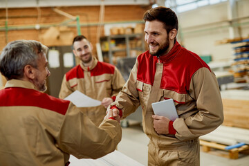 Wall Mural - Happy carpenter handshaking with is colleague while greeting in a workshop.