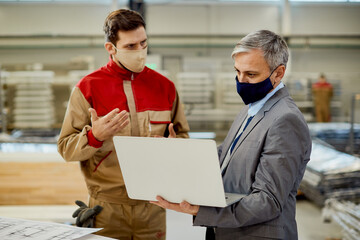 Wall Mural - Businessman and male worker using laptop while communicating at woodworking production facility.