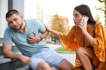 Canvas Print - Woman calling ambulance to help man with heart attack on stairs