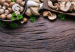 Different brown colored edible mushrooms on wooden table with herbs. Top view.