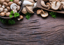 Different Brown Colored Edible Mushrooms On Wooden Table With Herbs. Top View.