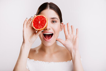 Sticker - Dark-haired lady with healthy skin looks into camera with smile, covering her eyes with red grapefruit