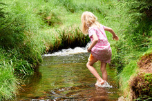 Child Cute Blond Girl Playing In The Creek. Gril Walking In Forest Stream And Exploring Nature. Summer Children Fun. Children Summer Activities