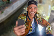 © MandriaPix - young african american man dressed street style taking a selfie, black man takes a picture with smartphone, influencer connecting with his fans with social network