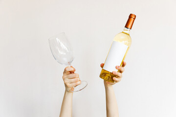 Human hands holding a wine glass and bottle of white wine on wall background.