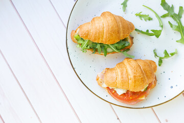 Two coissant with rocket salad and vegetables on a ceramic dish on a wooden table