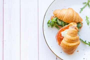 Two coissant with rocket salad and vegetables on a ceramic dish on a wooden table