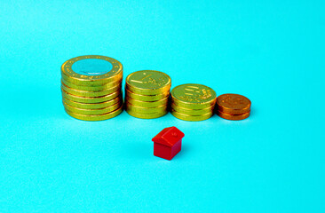 Sticker - High angle shot of coins stacked with a miniature house on blue background