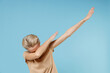 © ViDi Studio - Young blonde woman short haircut in casual basic beige t-shirt doing dab hip hop dance hands move gesture youth sign hiding covering face celebrating isolated on blue color background studio portrait.