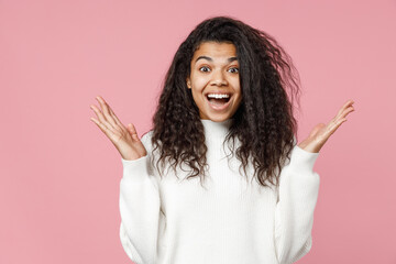 Young excited surprised attractive african american woman 20s curly hair wear white casual knitted sweater spreading hands isolated on pastel pink background studio portrait. People lifestyle concept.