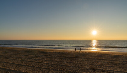 Wall Mural - people enjoy an evening walk on an empty golden sand beach at sunset