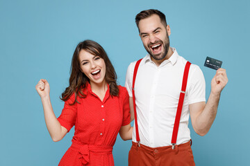 Sticker - Happy young couple two friends man woman wearing white red clothes hold credit bank card doing winner gesture isolated on pastel blue color background studio. St. Valentine's Day holiday concept.