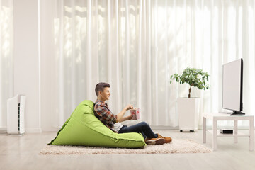 Poster - Teenager sitting on a bean bag armchair with a box of popcorn and watching tv in a minimal modern living room