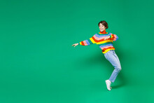 Full Length Side View Of Cheerful Funny Young Brunette Woman 20s In Basic Casual Colorful Sweater Dancing Standing On Toes Spreading Hands Isolated On Bright Green Color Background Studio Portrait.