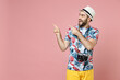 © ViDi Studio - Excited young traveler tourist man in summer clothes hat with photo camera point index fingers aside up isolated on pink background. Passenger traveling abroad on weekends. Air flight journey concept.