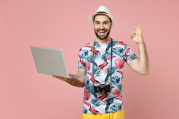 Wall Mural - Funny traveler tourist man in summer clothes hat work on laptop computer booking hotel showing ok okay gesture isolated on pink background. Passenger traveling on weekends. Air flight journey concept.