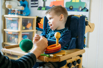 Activities for kids with disabilities. Preschool Activities for Children with Special Needs. Boy with with Cerebral Palsy in special chair play with mom at home.