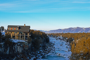 Poster - Mesmerizing view of a mountainous area with a frozen river, forest, and a modern house