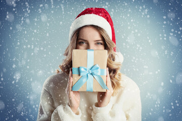 Sticker - Beautiful young woman in Santa hat with Christmas present on color background