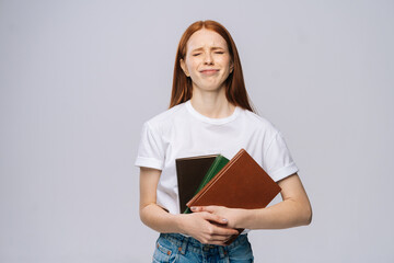 Displeased sad young woman college student holding book and crying on gray isolated background. Pretty redhead lady model wearing casual clothes emotionally showing facial expressions.