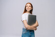 © dikushin - Smiling young woman student holding laptop computer and looking away on isolated gray background. Pretty lady model with red hair emotionally showing facial expressions in studio, copy space.