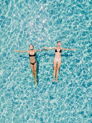 Couple of woman floating in clear blue sea. Aerial view