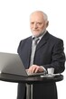 © nyul - Portrait of senior businessman using laptop on coffee table, eye contact, white background.