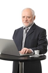 Poster - Portrait of senior businessman using laptop on coffee table, eye contact, white background.