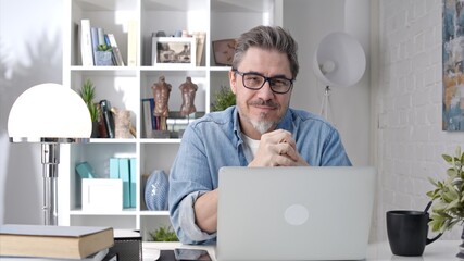 Older man working online with laptop computer at home sitting at desk. Home office, surfing internet, study room.