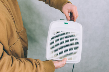 Wall Mural - A man holds a heater in his hands on a light background.