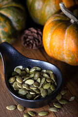 Wall Mural - Fresh peeled pumpkin seeds and pumpkins in a black bowl on wooden background. Close-up.