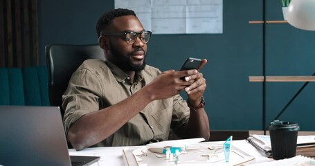young stylish architect using smartphone and smiling at office. happy businessman using mobile phone