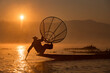 © Travel 'n' Lifestyle - INTHA FISHERMEN, INLE LAKE, SHAN STATE, MYANMAR - 18 January 2020: Traditional fishing technique balancing on one leg on a narrow boat using a conical net at sunrise.