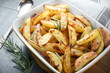 Roasted potatoes with rosemary in a baking dish on gray background.
