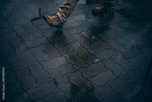 Fototapeta na szkło Man wearing brown shoes walking on a wet street with paving bricks pattern