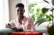 © Wavebreak Media - Portrait of african american woman sitting on couch drinking coffee looking at camera and smiling