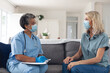 © Wavebreak Media - Senior african american female doctor talking with female patient both wearing face masks at home