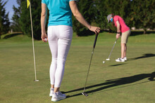 Two Caucasian Women Wearing Face Masks Playing Golf One Putting To The Hole