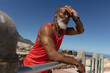 © Wavebreak Media - Fit senior african american man wearing earphones in sun by sea mopping brow