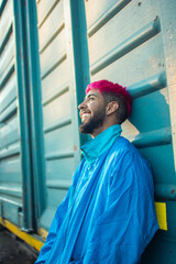 Young man with stylish pink-dyed hair wearing a retro jacket leaning against a railway wagon